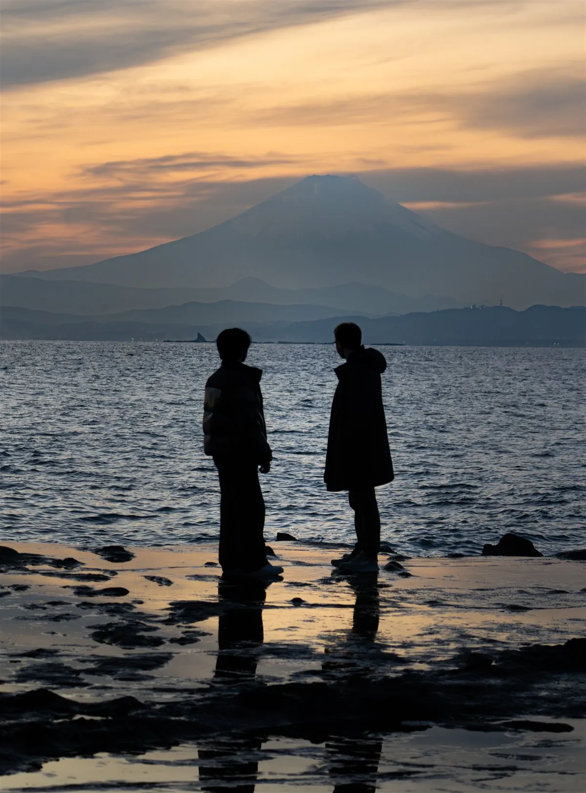 Me and my friend standing by the sea in front of Mount Fuji at sunset